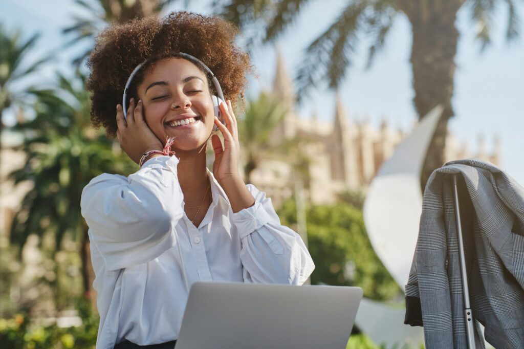 Black female freelancer in headphones and with netbook on street